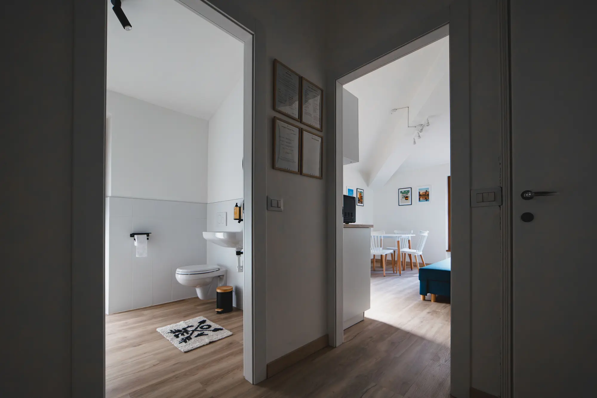 Hallway view showing the bathroom on one side and the living area with dining table on the other
